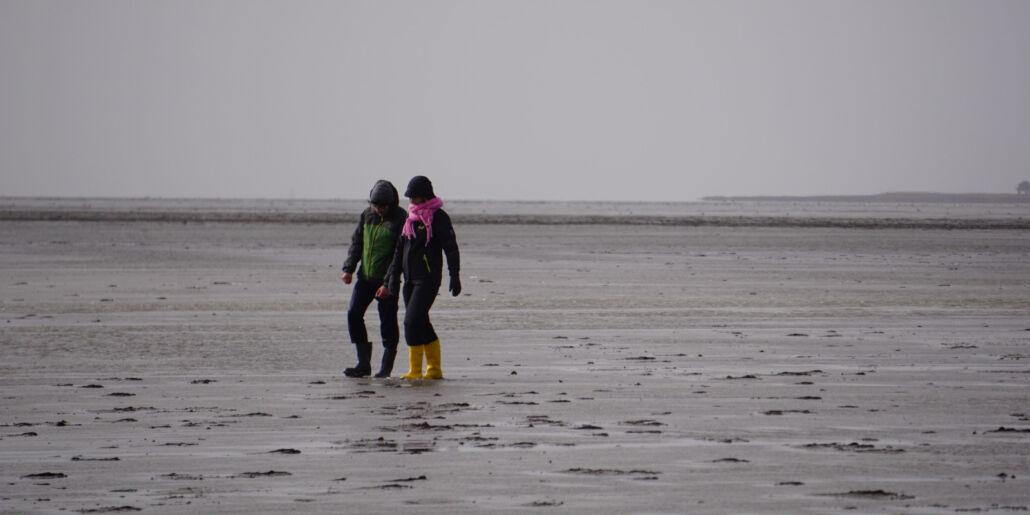 Zwei Personen mit gelben Gummistiefeln wandern bei Regen am Strand von Kiel, wo sich GEOMAR Studierende auf das GAME-Porgramm, dass auch an der Meeresschule stattfindet, vorbereiten